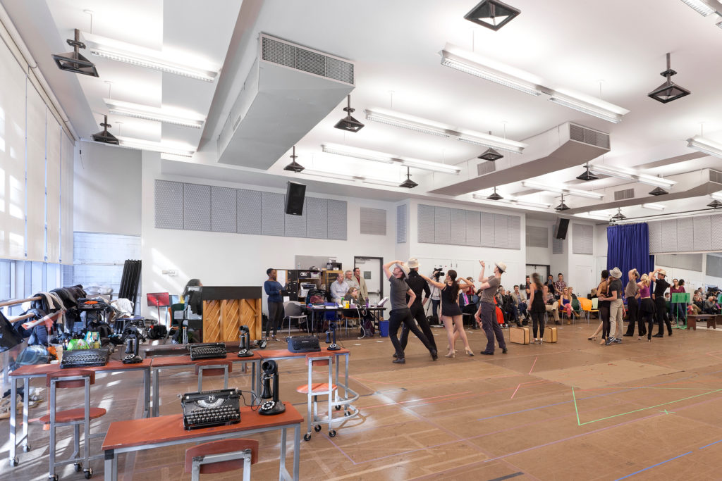 Broadway actors and dancers rehearse a western-style dance number in a rehearsal studio.