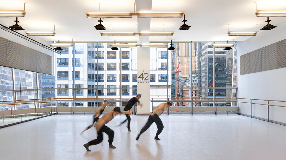 Four dancers mid-movement rehearse in an empty studio.