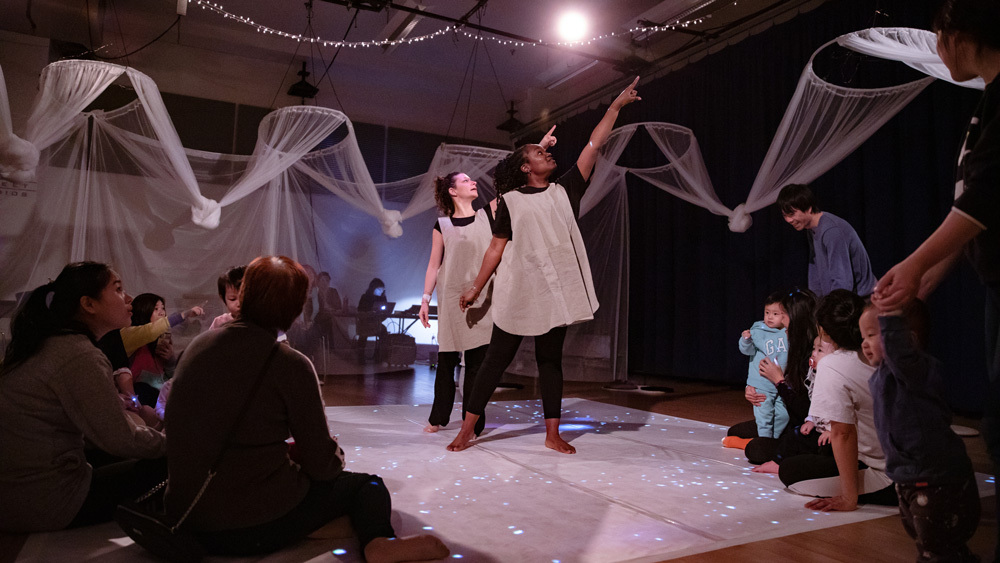 Two actors from Spellbound Theatre's Shakespeare's Stars point up, capturing the attention of a surrounding group of babies and parents.