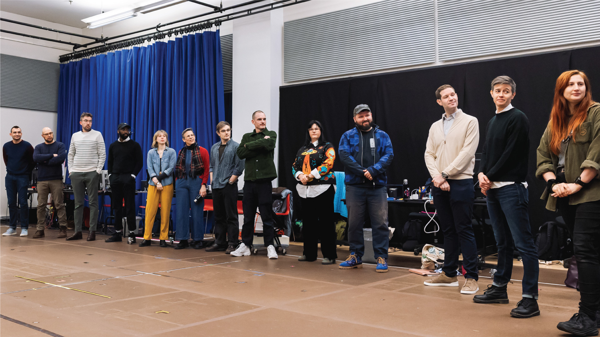 A dozen people standing in a line with arms folded or clasped facing someone