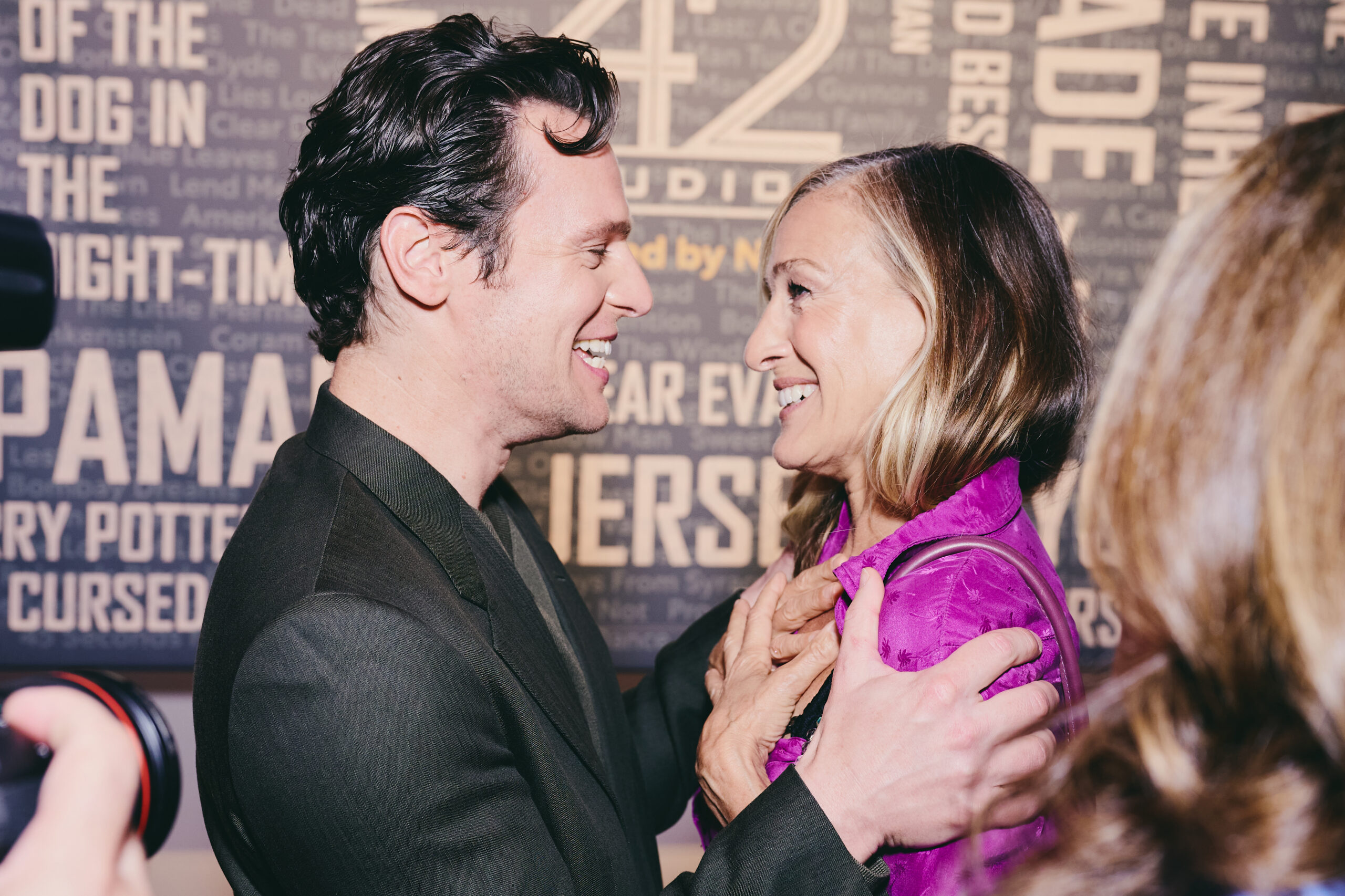 Jonathan Groff faces Sarah Jessica Parker and holds her shoulders as they look into each others' eyes and smile